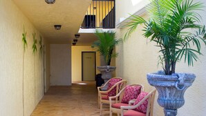 A corridor with stone flooring, wicker chairs with red cushions, and potted plants. - At Home Inn (Fort Pierce)