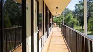 A covered corridor with wooden flooring, glass doors, and a metal railing. - At Home Inn (Fort Pierce)
