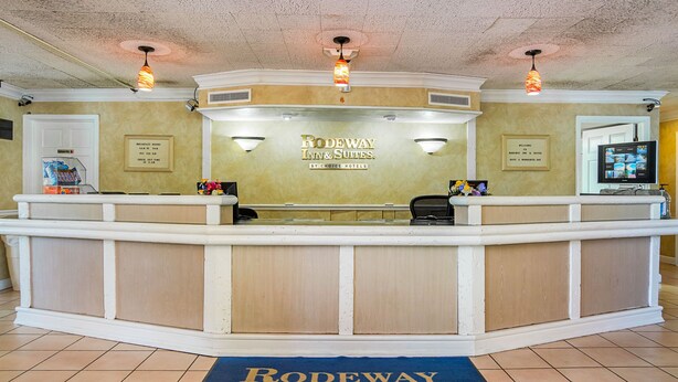 A reception desk at Rodeway Inn & Suites with a blue carpet, a TV screen, and a framed welcome sign. - Rodeway Inn and Suites (Little Rock)