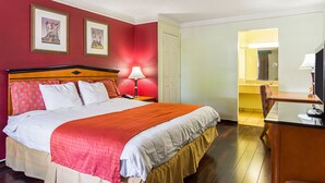A hotel room with a bed, a desk with a lamp, a chair, and a bathroom visible through an open door. - Rodeway Inn and Suites (Little Rock)