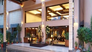 A hotel entrance with a covered patio, large windows, and potted plants. - Jukaso IT Suites (Gurugram)