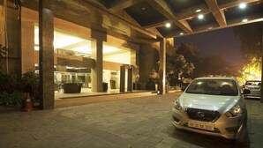 A modern building with a covered entrance, a car parked in front, and a well-lit interior. - Jukaso IT Suites (Gurugram)