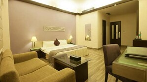 A hotel room with a bed, two bedside tables, a desk, a chair, and a sofa. - Jukaso IT Suites (Gurugram)