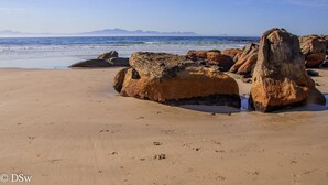 A sandy beach with large rocks and a clear view of the ocean and distant mountains. - Lark House, Peaceful Mountain Home with Amazing Ocean Views (Cape Town)