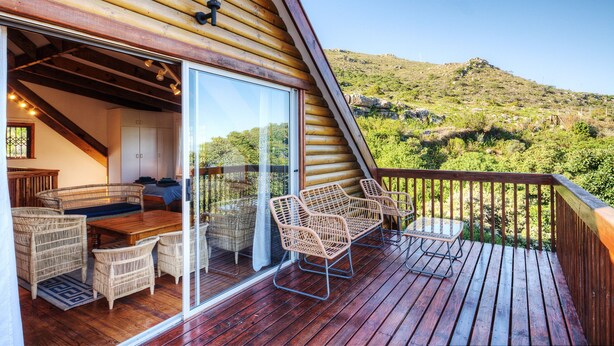 A wooden deck with wicker furniture and a glass door leading to a room with a view of a green landscape. - Lark House, Peaceful Mountain Home with Amazing Ocean Views (Cape Town)