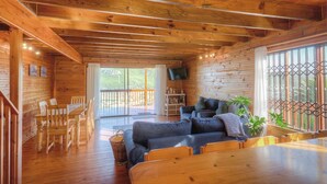 A wooden cabin interior with a dining area, sofa, and a TV mounted on the wall. - Lark House, Peaceful Mountain Home with Amazing Ocean Views (Cape Town)