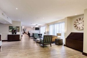 A hotel lobby with a wooden floor, seating area with chairs and a sofa, a large wall clock, and a flat-screen TV mounted on the wall. - Quality Inn Gulfport I-10 (Gulfport)