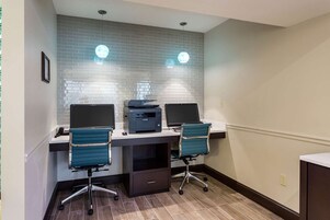 Un espacio de oficina moderno con dos escritorios, cada uno con una computadora portátil y una impresora, y dos sillas de oficina azules.