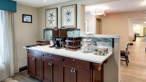 A modern kitchen with dark wood cabinets, a white countertop, and a backsplash with blue tiles. There are framed starfish decorations on the wall, and a coffee maker on the counter. - Quality Inn Gulfport I-10 (Gulfport)