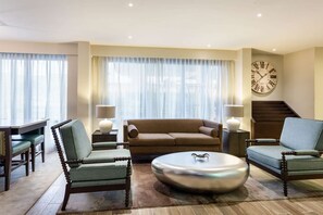A living room with a sofa, two armchairs, a coffee table, a dining table, and a clock on the wall. - Quality Inn Gulfport I-10 (Gulfport)