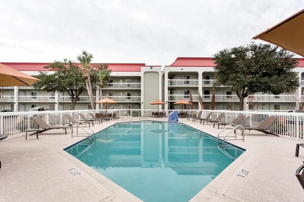 A swimming pool with lounge chairs and umbrellas, surrounded by a white fence and a building with balconies. - Quality Inn Gulfport I-10 (Gulfport)