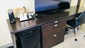 Ein Hotelzimmer mit dunklem Holzschreibtisch, Fernseher, Kaffeemaschine, Minikühlschrank und Stuhl.