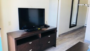 Ein modernes Wohnzimmer mit einem Flachbildfernseher auf einer Holz-Unterhaltungsanlage, einem Spiegel an der Wand und einer Tür zu einem weiteren Raum.