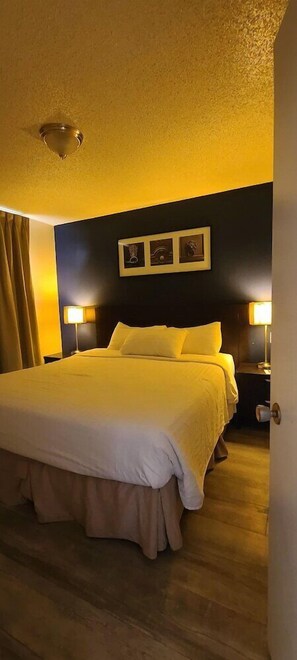 Habitación de hotel con una cama grande, dos lámparas de noche, un cabecero oscuro y un cuadro enmarcado sobre la cama.