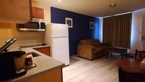 Eine kompakte Küche mit Mikrowelle, Kühlschrank und Kaffeemaschine. Im Wohnbereich befindet sich eine Couch und ein Esstisch.