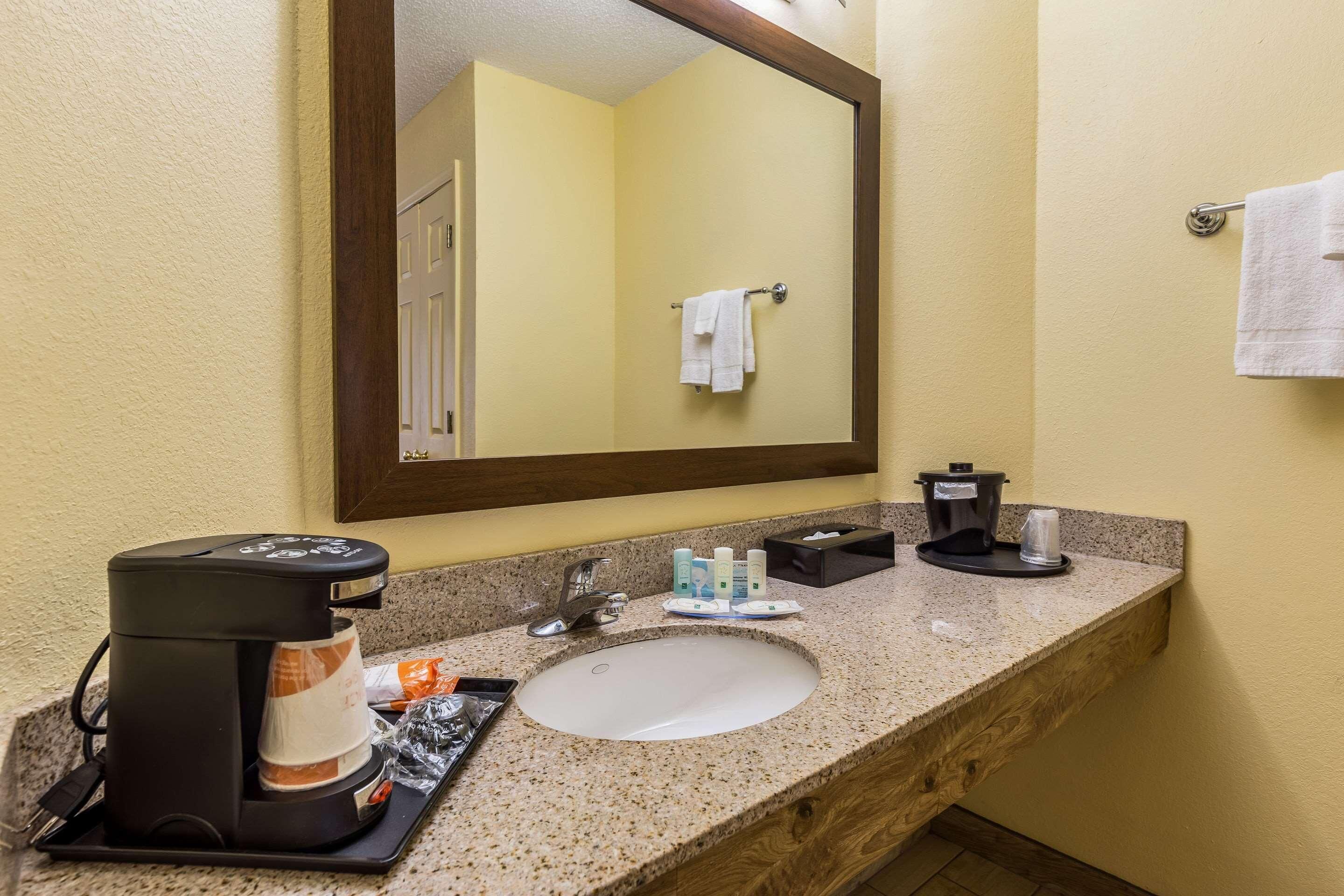 A hotel bathroom with a granite countertop, a sink, a coffee maker, and toiletries.