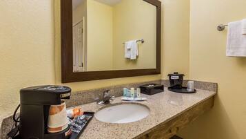 A hotel bathroom with a granite countertop, a sink, a coffee maker, and toiletries.