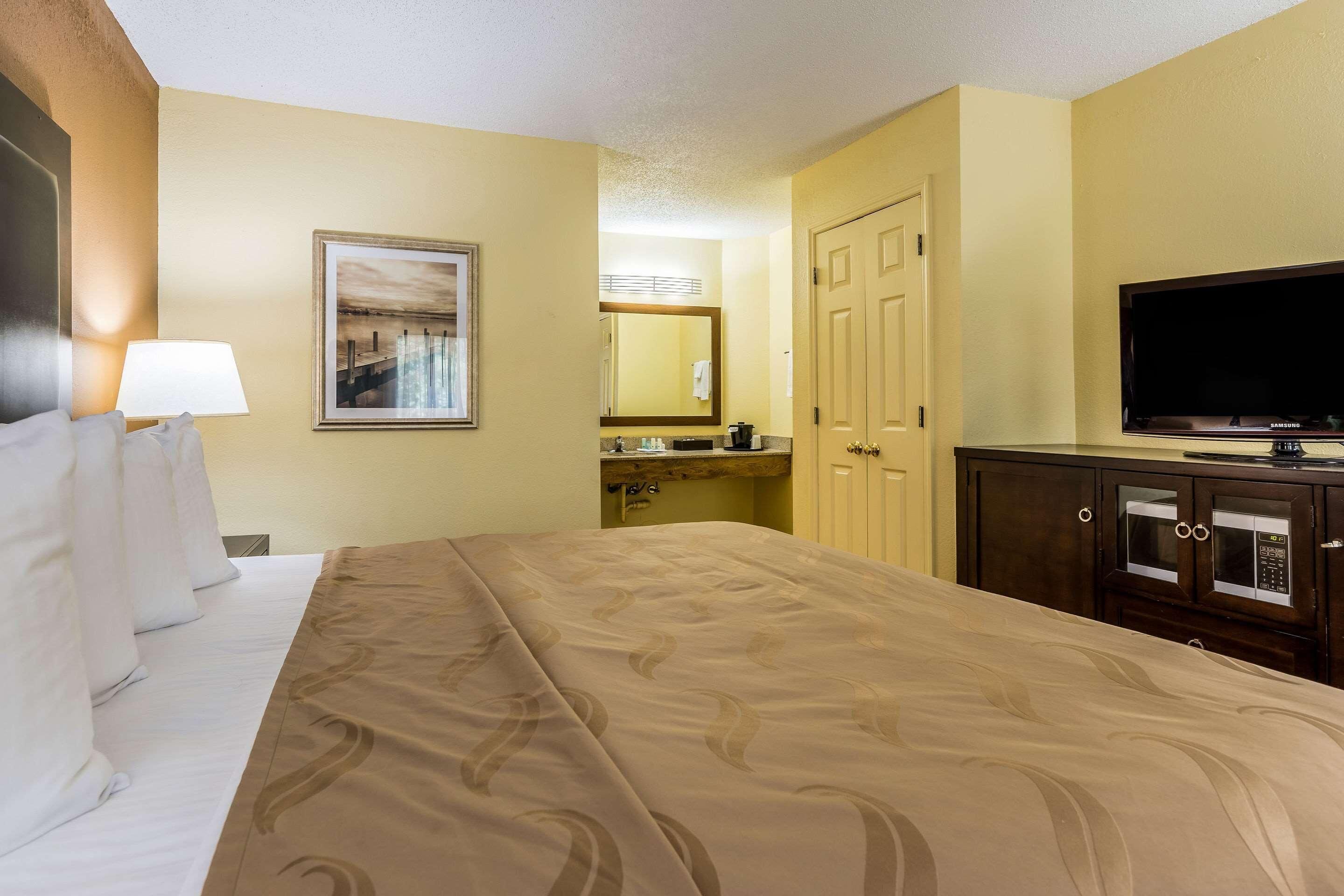 A hotel room with a bed, a television, a desk with a lamp, a mirror, and a door.
