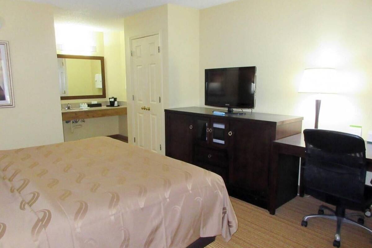 A hotel room with a bed, a desk with a television, a chair, a dresser, and a mirror.