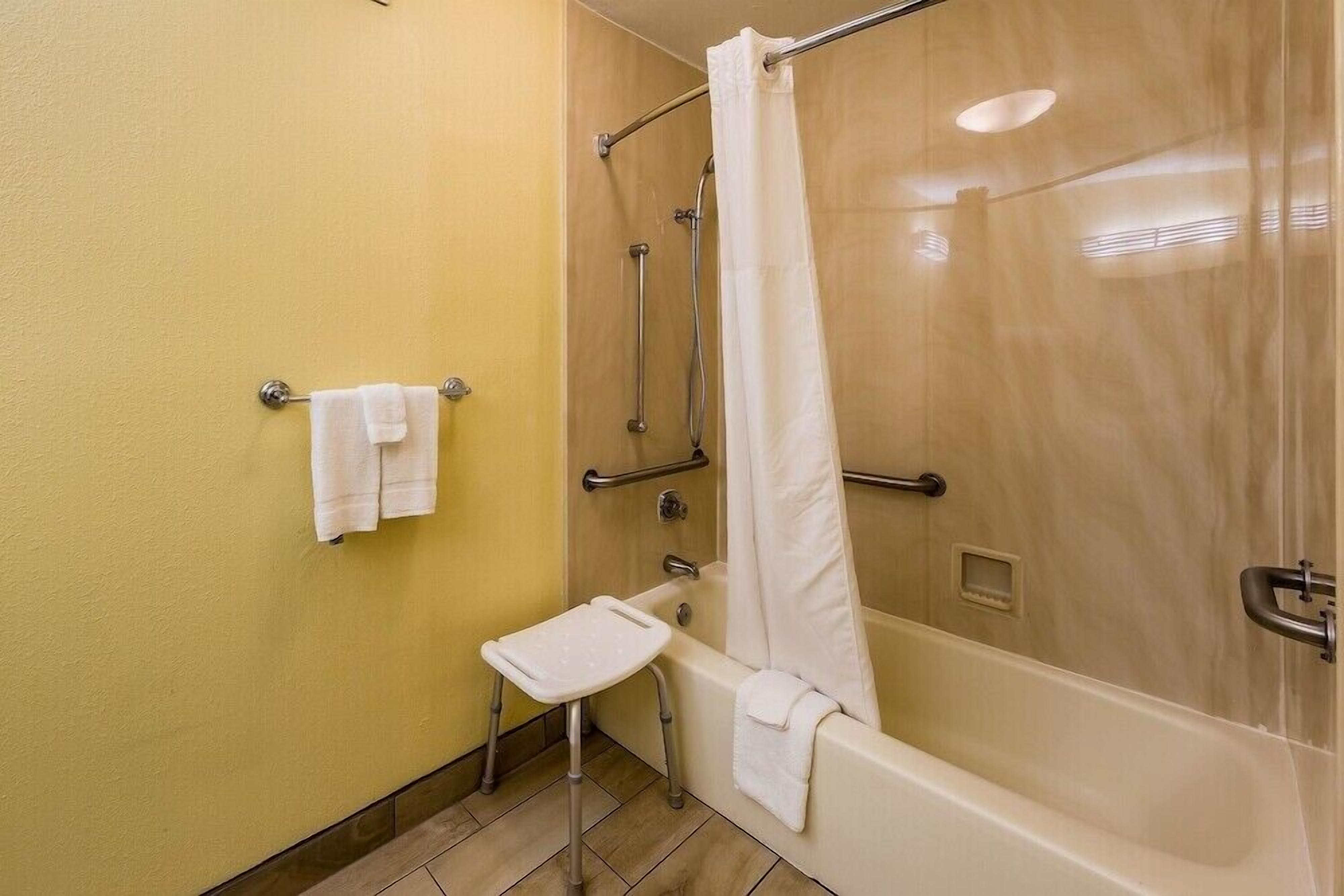 Een badkamer met een badkuip, een douche met gordijn, een klein krukje en een handdoekhouder.