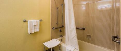Een badkamer met een badkuip, een douche met gordijn, een klein krukje en een handdoekhouder.