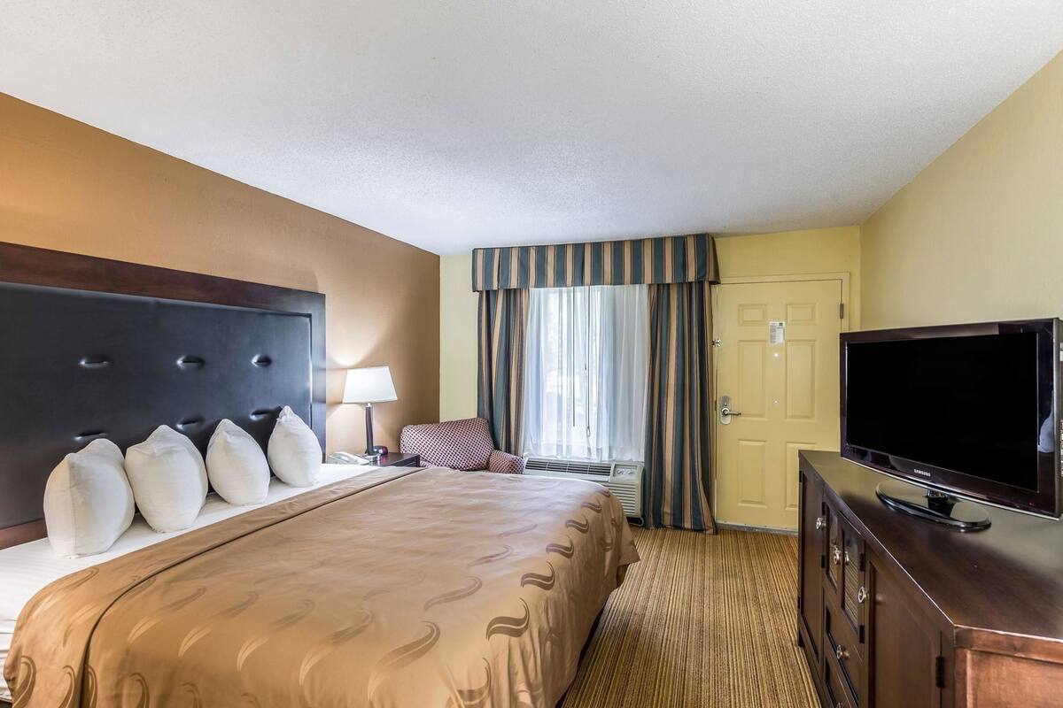 A hotel room with a large bed, a TV, a desk, and a door.