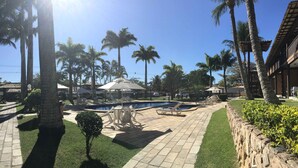 A pool area with lounge chairs and umbrellas, surrounded by palm trees and a stone pathway. - Cozy property just a 3-minute walk from the beach (Free Wifi Room Service) (Buzios)