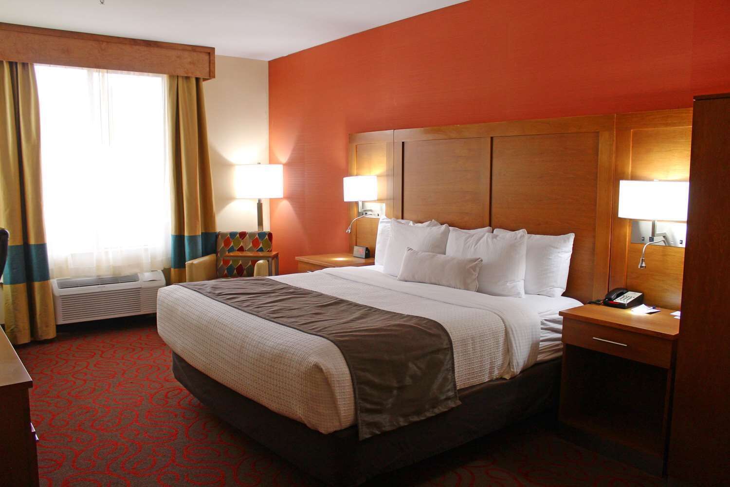 Une chambre d’hôtel avec un grand lit, deux tables de chevet avec des lampes, un bureau, une chaise et une fenêtre avec des rideaux.