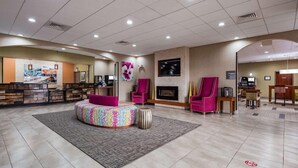 Un vestíbulo de hotel con mostrador de recepción, chimenea, zona de estar con sillones y televisor.