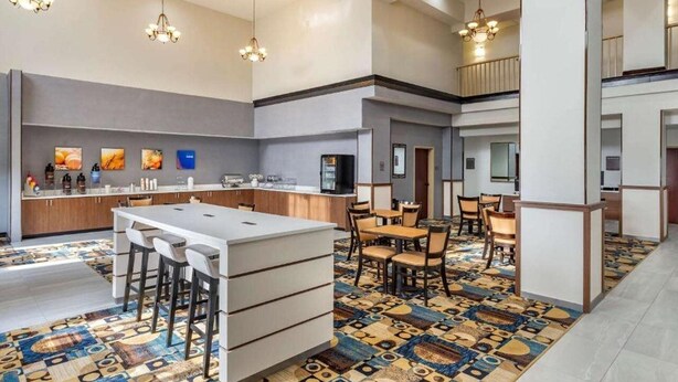 Un moderno hall de hotel con una zona de bar central, rincones de estar y una alfombra estampada.