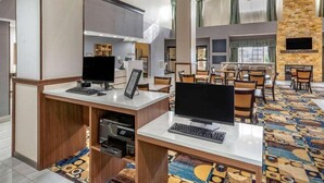 Un vestíbulo de hotel con mostrador de recepción, computadoras y un área de descanso con sillas y mesas.