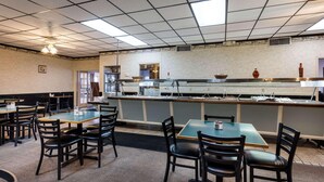 A dining area with tables and chairs, a counter with food items, and a ceiling with fluorescent lights. - Econo Lodge (Osceola)