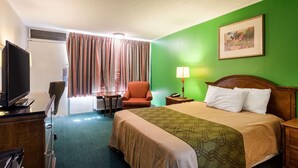 A hotel room with a bed, a desk, a chair, a television, and a window with curtains. - Econo Lodge (Osceola)