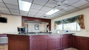 A kitchen with a wooden island, a window with curtains, and a red rug with a logo. - Econo Lodge (Osceola)
