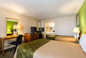 Quarto de hotel com cama, escrivaninha, computador, cadeira, televisão e guarda-roupa.