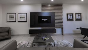 A modern living room with a flat-screen TV, framed artwork, and a minimalist design. - Clarion Inn & Suites (Mission)