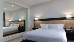A modern hotel room with a large bed, bedside tables, a mirror, and a bench. - Clarion Inn & Suites (Mission)