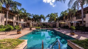 A swimming pool surrounded by palm trees and outdoor seating areas. - Clarion Inn & Suites (Mission)