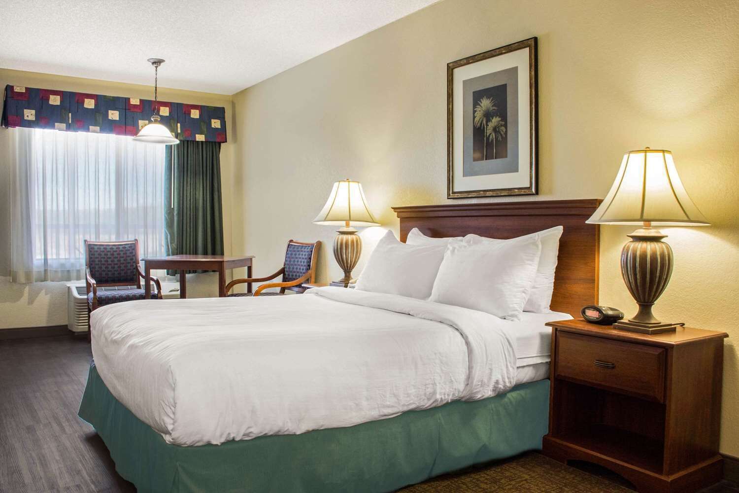 A hotel room with a large bed, two bedside tables with lamps, a chair, a desk, and a window with curtains.