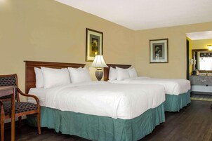 Habitación de hotel con dos camas, una silla, una mesita de noche con lámpara y cuadros en la pared.