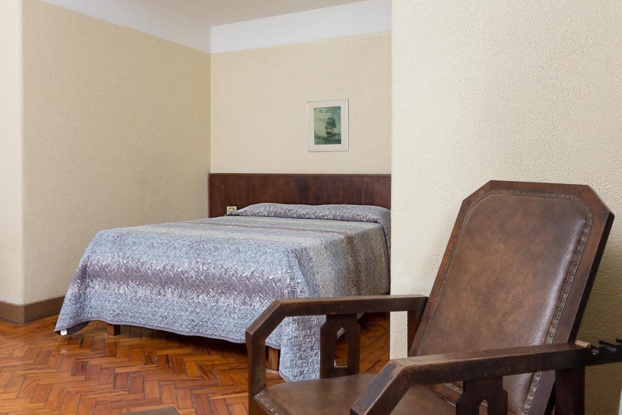 Une pièce comprenant un lit, une chaise en bois et un tableau encadré accroché au mur.