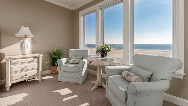 Une chambre avec vue sur la plage, un fauteuil blanc, une petite table avec une lampe et une commode.