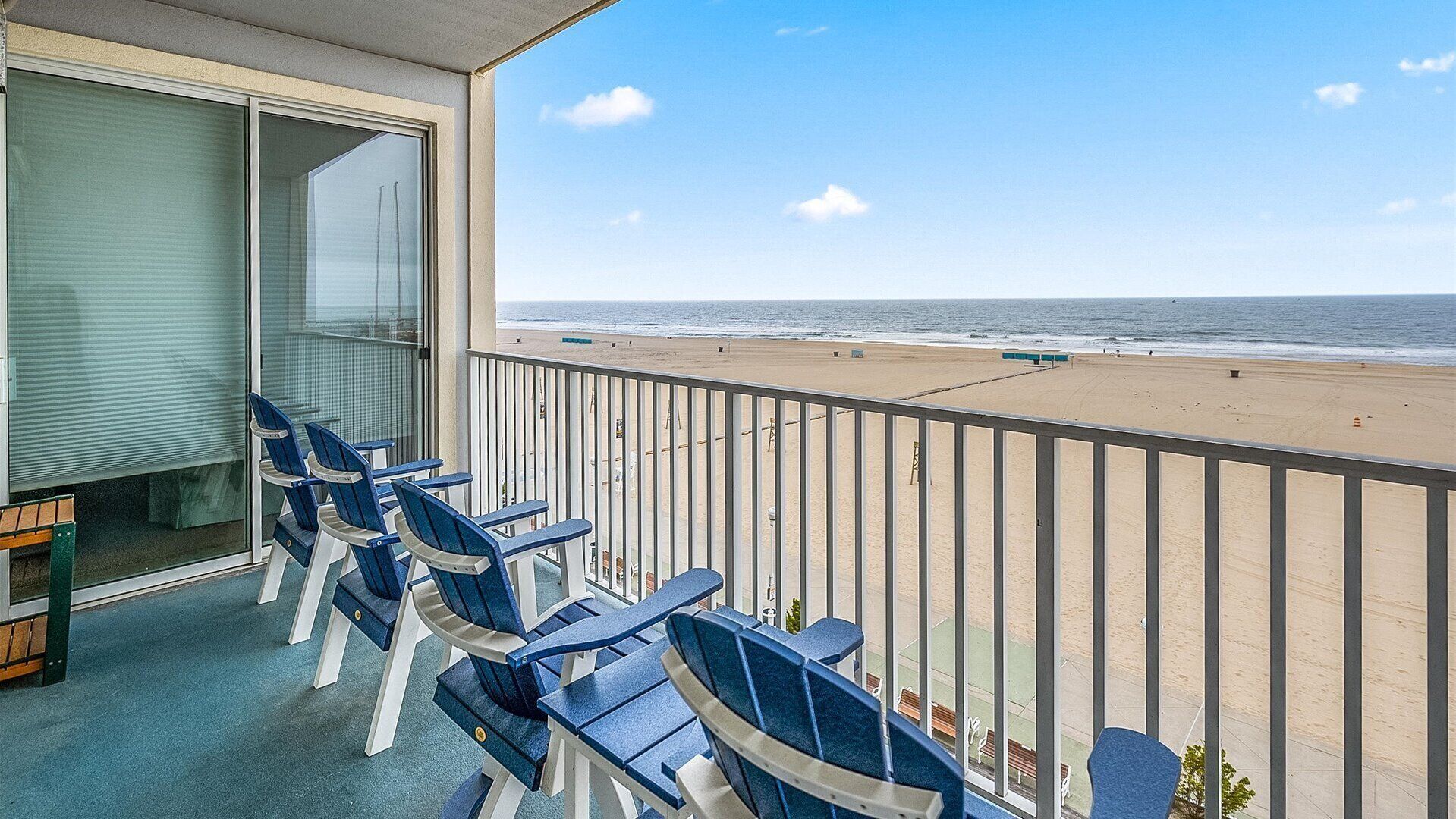A balcony with blue chairs and a view of the beach.