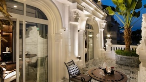 Une terrasse extérieure luxueuse, agrémentée de colonnes blanches décorées, d’un sol carrelé à motifs et d’une table avec des chaises.