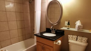 Un baño con bañera, lavamanos, espejo, inodoro y papel higiénico.