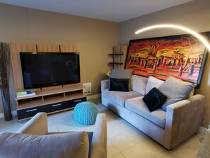 A modern living room with a flat-screen TV, a sofa, and a large painting on the wall.