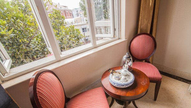 A corner room with a window, two striped chairs, a small round table with a teapot and cups, and a view of buildings and trees outside. - Xiamen Yunpin Hotel (Xiamen)