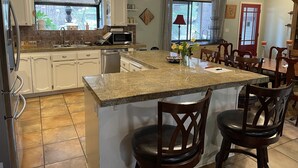 Una cocina con armarios blancos, encimera de granito y una isla central con dos taburetes de bar.
