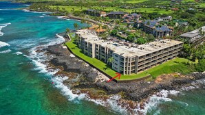 A coastal hotel with multiple buildings, a rocky shoreline, and clear turquoise waters. - Kuhio Shores Oceanfront Corner Unit (Koloa)