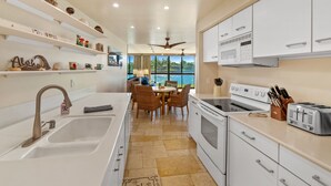 A modern kitchen with white cabinetry, a large island, and a view of the outdoors. - Kuhio Shores Oceanfront Corner Unit (Koloa)